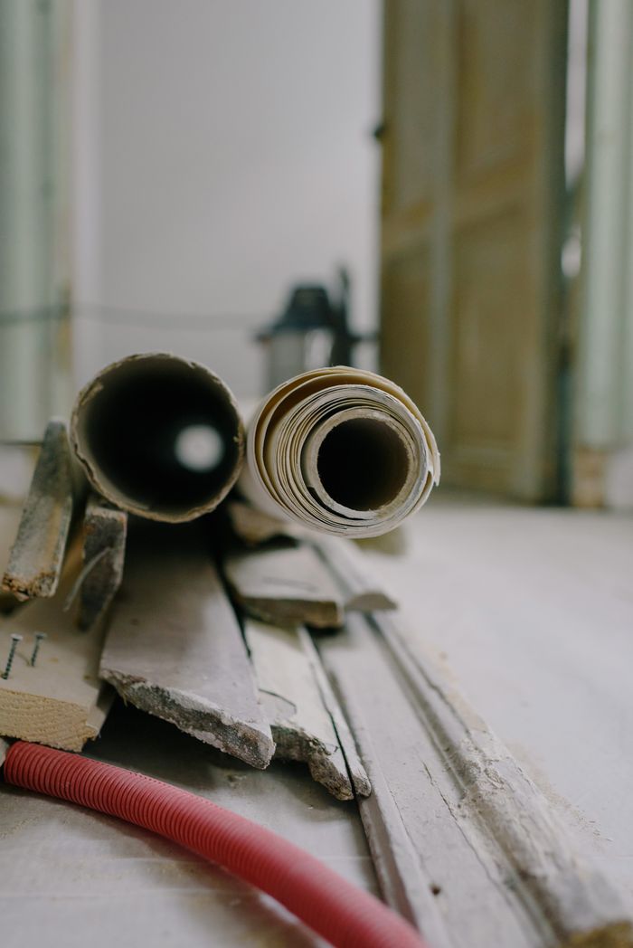about-us Pile of wooden planks and rolls on floor near open door in flat during renovation