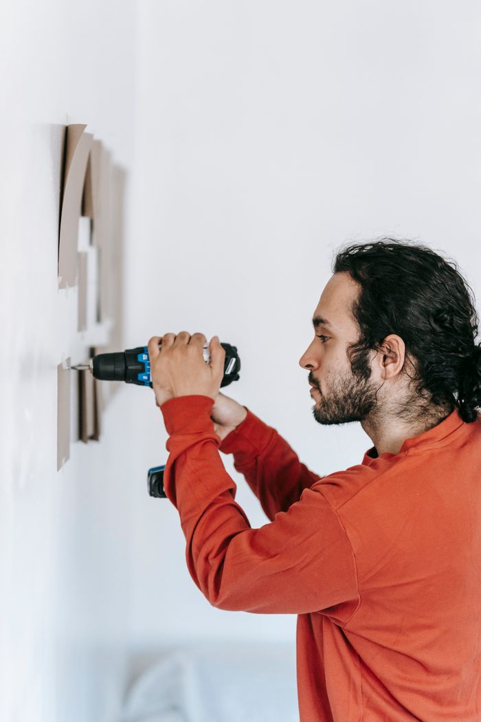 about-us Focused man drilling into wall, enhancing home interiors with precision tools.