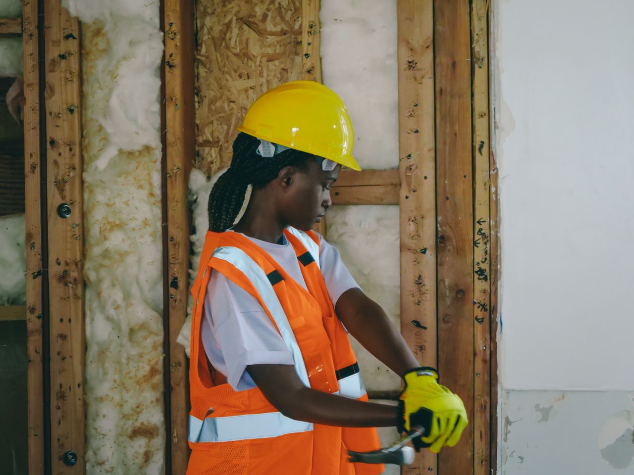 services-01 Female construction worker in PPE hammering indoors on a renovation site.